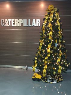 a large christmas tree with yellow ribbon around it in front of a caterpillar sign