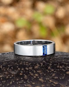 a wedding band with a blue stone in the center on top of a piece of wood