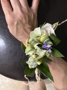 a woman's hand is holding a bouquet of white and purple flowers with green leaves