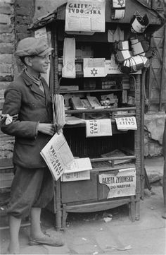 an old black and white photo of a man standing in front of a newspaper stand