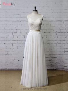 a white wedding dress on a mannequin stand in front of a brick wall