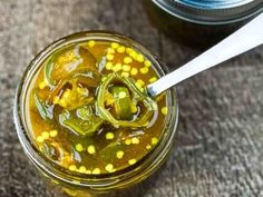 pickled peppers and corn in a jar with a spoon next to it on a table