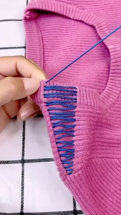 someone is stitching the back of a pink sweater with blue thread on it,