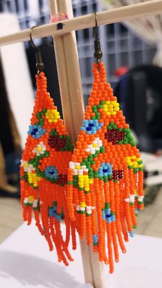 an orange beaded earring hanging from a wooden stand in front of a building