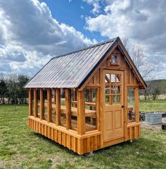 a small wooden shed with a metal roof and windows on the side, in a grassy field