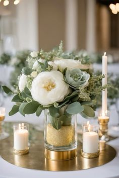 a vase filled with white flowers and greenery on top of a gold plated table