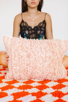 a woman sitting in front of a pillow on top of an orange and white blanket