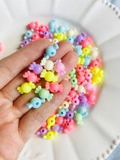 a hand is holding some tiny beads on a white plate with pink and blue flowers