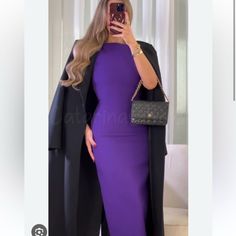 a woman in a purple dress taking a selfie with her cell phone while wearing a black coat