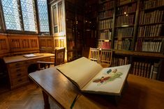 an open book sitting on top of a wooden table in front of a library filled with books