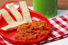 a red plate topped with crackers next to a green cup on a tablecloth