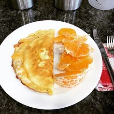 a white plate topped with an omelet covered in orange slices next to silverware