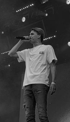 a man standing on top of a stage with a microphone in his hand and wearing a white t - shirt