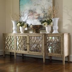 an ornate sideboard with vases and flowers on it in front of a window