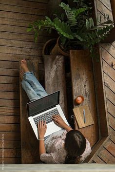 a woman sitting on the floor using a laptop computer with her feet propped up in a wooden crate