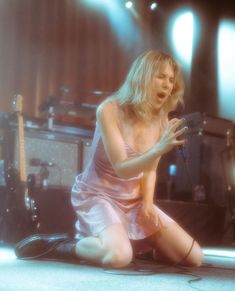 a woman sitting on the ground in front of a microphone with her hands out and legs crossed