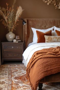 a bed with pillows and blankets on it in a bedroom next to a dresser, lamp and vase