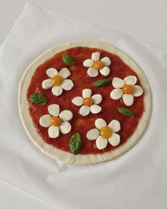 a small pizza with flowers on it sitting on top of a white table cloth covered in wax paper