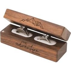 two wedding rings in a wooden box with mountains on the top and below it, sitting next to each other