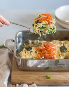 a person is taking a slice of vegetable lasagna out of the casserole dish