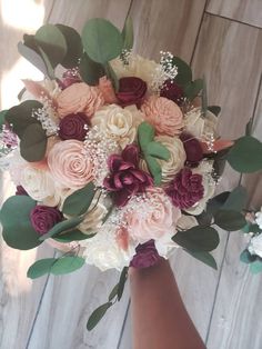 a bridal bouquet with pink, red and white flowers on it is held by someone's hand