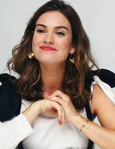 a woman sitting at a table with her hands folded in front of her chest and wearing gold earrings