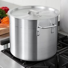 a stainless steel pot sitting on top of a stove next to a cutting board with vegetables