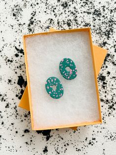 two green donuts sitting in a box on top of a white countertop with black speckles