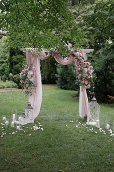 an outdoor wedding setup with pink and white flowers on the arch, candles and lanterns