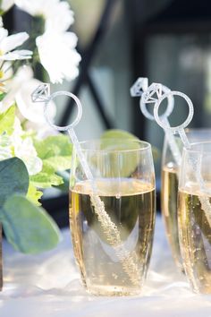 two champagne flutes are sitting next to each other on a table with flowers in the background