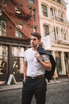 a man standing in front of a building wearing a white shirt and black pants with a backpack on his back