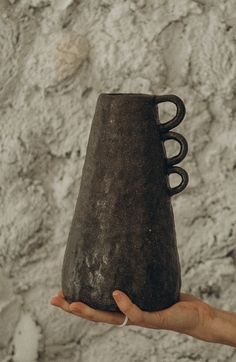 a hand holding a black vase in front of a stone wall