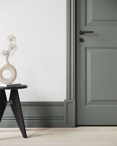 a vase sitting on top of a black table next to a gray door and white wall