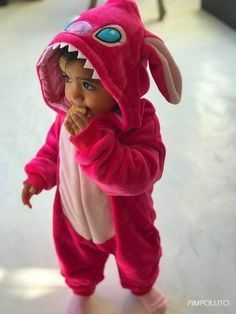 a small child in a pink dinosaur costume eating something with his mouth open and teeth out