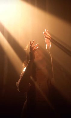 a woman is holding her hands up in the air with light shining on her face