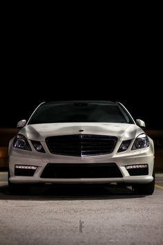 the front end of a white car parked on top of a parking lot at night