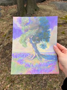 a person holding up a piece of paper with a painting on it in front of a tree