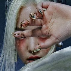 a woman with white hair and piercings holding her hand up to her face while wearing gold rings