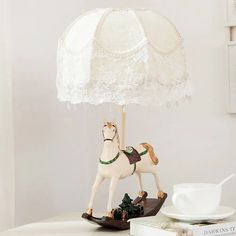 a white horse figurine holding an umbrella on top of a table next to a cup and saucer