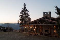 a rustic cabin sits in the middle of a field at dusk with mountains in the background