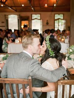 a bride and groom kissing in front of a large group of people at a dinner table