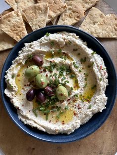 hummus and olives in a blue bowl with pita chips on the side