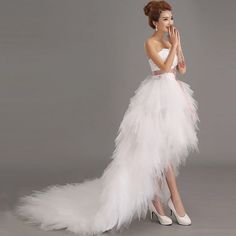 a woman in a white dress with feathers on the skirt and heels is posing for a photo