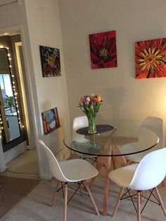 a glass table with four white chairs and flowers on it in front of a doorway