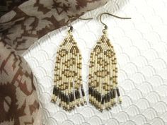 two pairs of beaded earrings on top of a white cloth covered tablecloth with a brown and black design