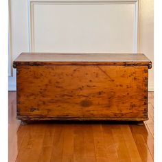 an old wooden chest sitting on top of a hard wood floor next to a white wall