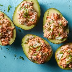 four stuffed avocados with tuna salad in them on a blue surface, top view