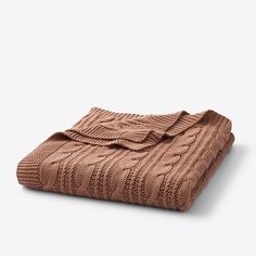 a brown blanket folded on top of a white surface with an open knitted design