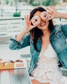 a woman sitting at a table with two donuts in front of her eyes and one on the other side