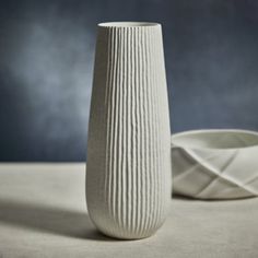 a white vase sitting on top of a table next to a bowl